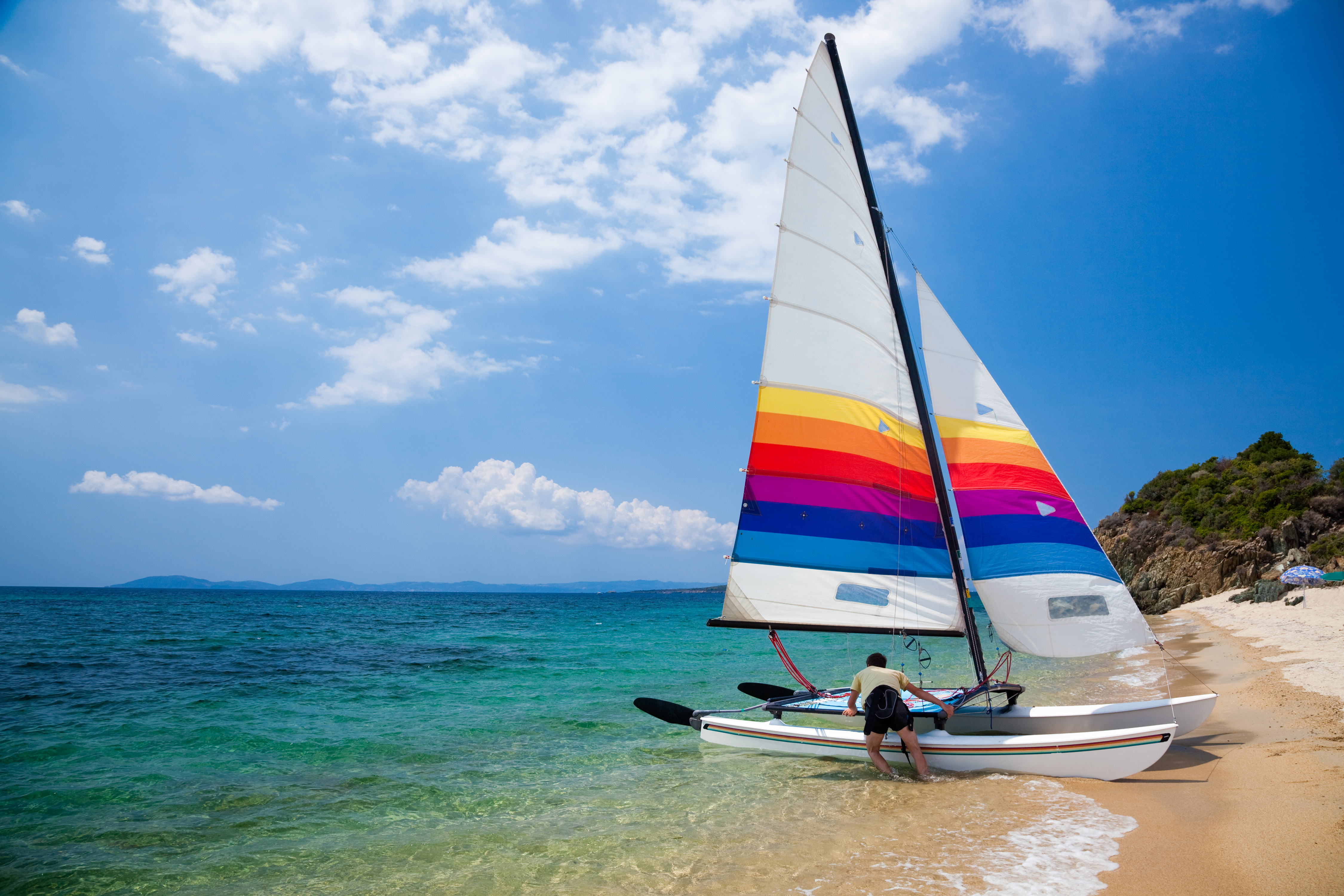 Delta Vacations catamaran with a colorful striped sail on a tropical beach